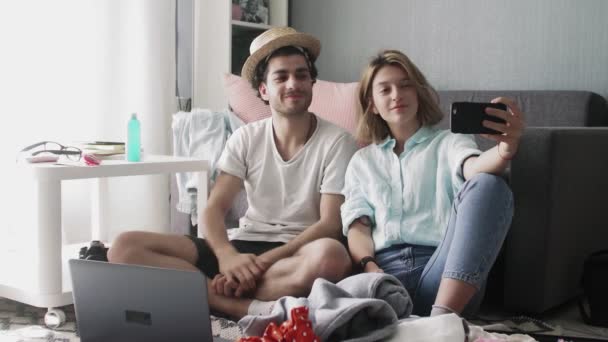 スーツケースや服を背景に自撮りをしている若いカップル。夏休みの準備 — ストック動画