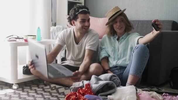 Een meisje met een hoed en een man met een laptop opnemen video op de telefoon voor het reizen — Stockvideo
