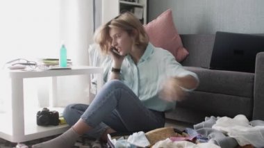 Genç bir kadın evde bavulunu topluyor, yolculuk için hazırlanıyor, bavulları hazırlıyor ve akıllı telefondan konuşuyor.