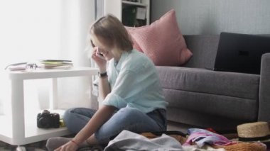 Tatlı kız yolculuk için hazırlanıyor, bavulları hazırlıyor ve akıllı telefondan konuşuyor.