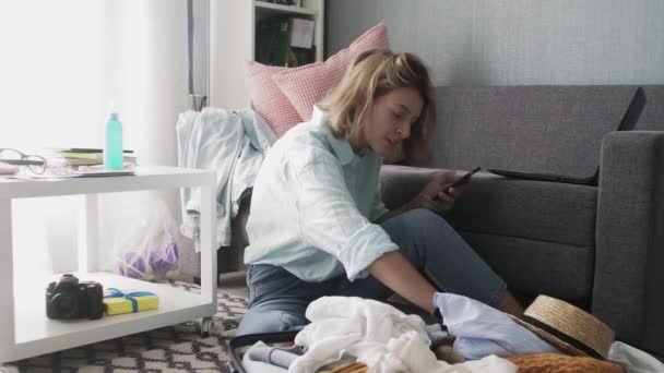 Une jeune fille avec un téléphone dans ses mains vérifie une liste de choses à voyager et envoie des SMS à des amis — Video