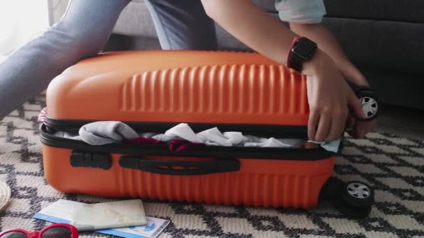 Mujer linda de pie sobre sus rodillas en la maleta naranja sobrecargada y tratando de cerrarlo — Vídeo de stock