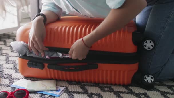 Jeune fille debout sur le coude sur une valise orange surchargée, essayant de la fermer — Video