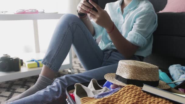 Une jeune fille près d'une valise de voyage regarde les réseaux sociaux sur le smartphone, bavarder avec des amis — Video