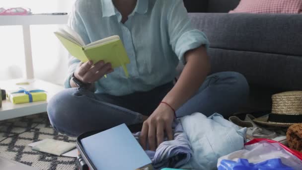 Chica joven con un cuaderno en sus manos comprueba la lista de ropa para las vacaciones — Vídeo de stock