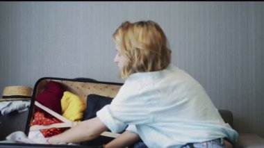 Kanepede oturan ve bavulunu hazırlayan gezgin kadının yan görüntüsü.