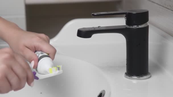 Giovane donna lavarsi i denti con uno spazzolino da denti in bagno. Primo piano delle mani che stringono la pasta sul pennello — Video Stock