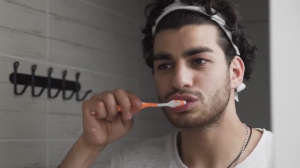 Baard man poetsen zijn tanden in de voorkant van spiegel in badkamer — Stockvideo