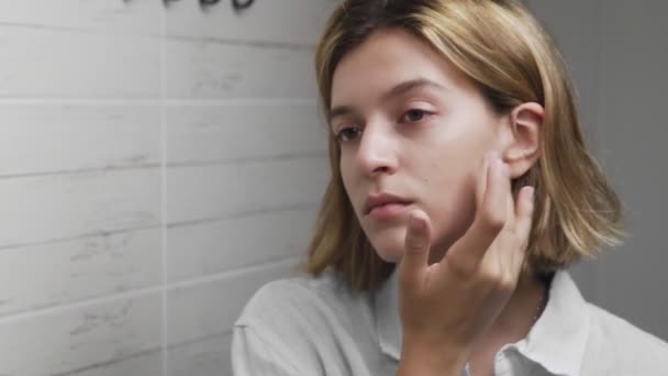 Mujer joven aplicando crema y mirando en el espejo disfrutar de la belleza natural y saludable — Vídeo de stock