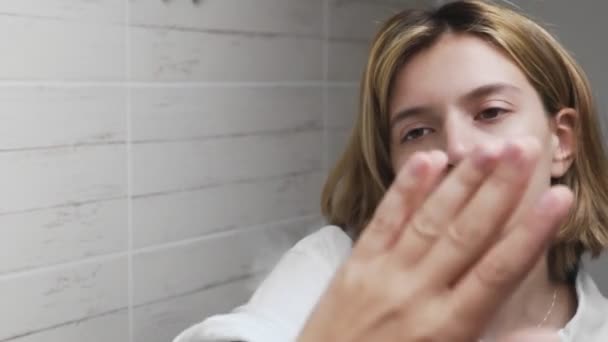 Молодая женщина чистит зеркало рукой — стоковое видео