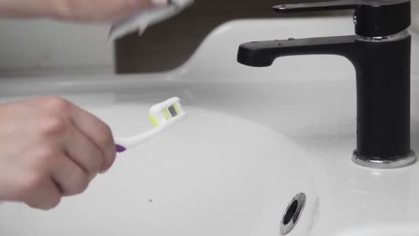 Young woman brushing teeth with a tooth brush in bathroom. Close-up of hands squeezing pasta on the brush — Stock Video