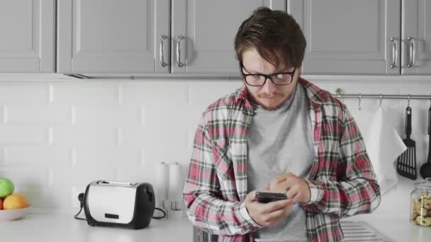 Joven hombre atractivo utilizar el teléfono en la cocina en casa — Vídeo de stock