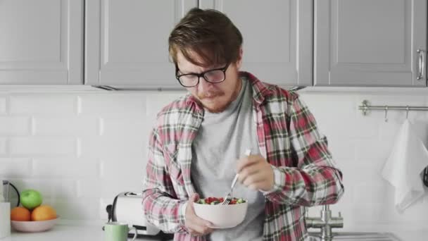 Homem com óculos está comendo salada dieta helthy na cozinha — Vídeo de Stock