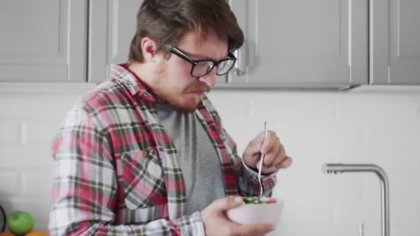Mannen med glasögon äter helhetssallad i köket. — Stockvideo
