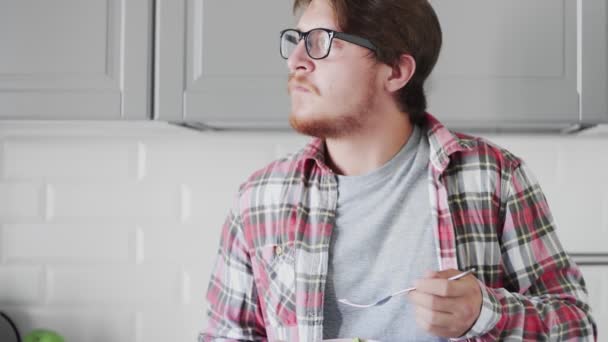 Mannen med glasögon äter helhetssallad i köket. — Stockvideo