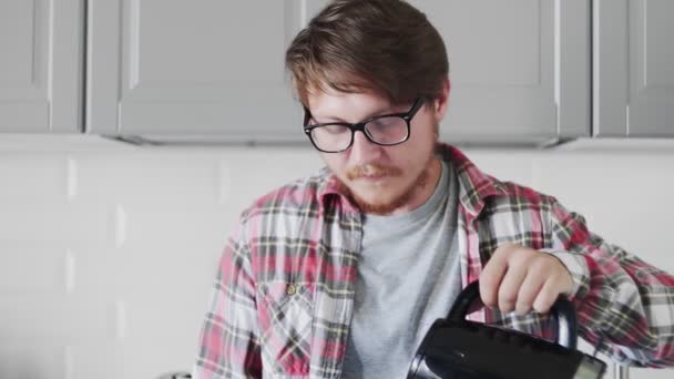 Young man using phone and drinking coffee while sandng in the kitchen — Stock Video