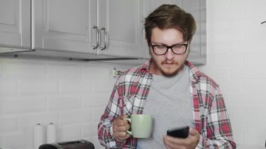 Elinde çay olan genç adam evde telefonla konuşuyor.