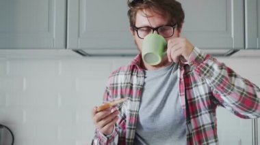 Genç adam çilek reçelli tost yiyor ve kahve ya da çay içiyor.