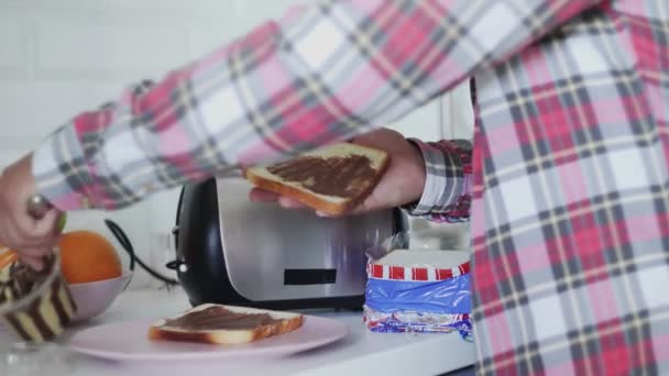 Muž dělá snídani, když rozmaže čokoládovou pomazánku na toast. — Stock video