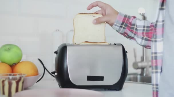 Bir adam ekmek kızartma makinesine ekmek koyar. Ekmek kızarmış. Kahvaltılık yemek hazırlanıyor. Mutfakta elektrikli alet var. — Stok video
