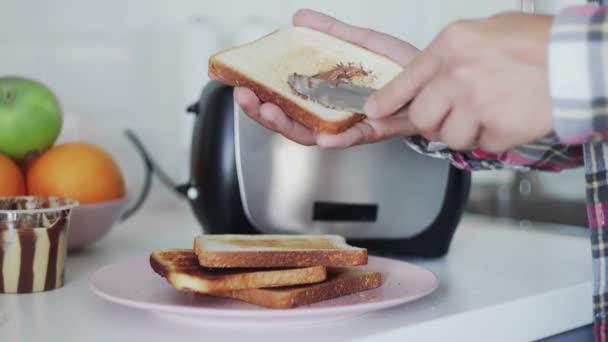 Hombre haciendo el desayuno mientras se extiende pasta de chocolate en tostadas. — Vídeo de stock