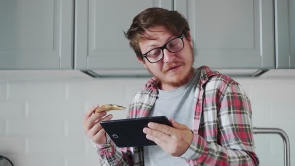 Jeune homme avec tablette manger du pain grillé avec de la pâte de chocolat. Homme regarder une vidéo drôle sur tablette et rire — Video