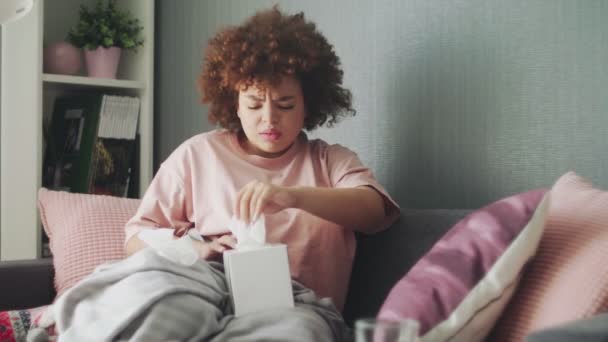 Sick african american girl with flu virus on sofa at home. She uses wipes to sneeze — Stock Video