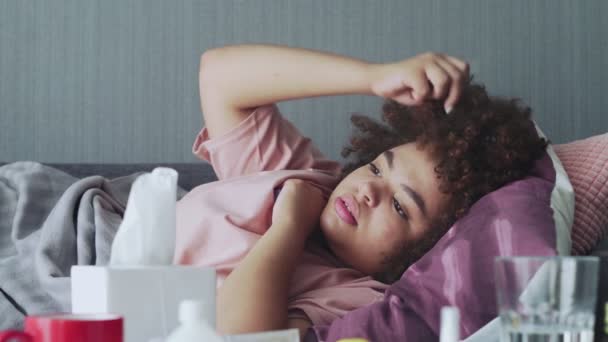 Niña afroamericana enferma con gripe acostada en el sofá en casa. Enferma joven mujer negra con temperatura de comprobación en frío con termómetro — Vídeo de stock