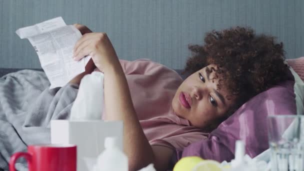 Enfermo afroamericano chica toma pastillas con agua, acostado en el sofá . — Vídeo de stock