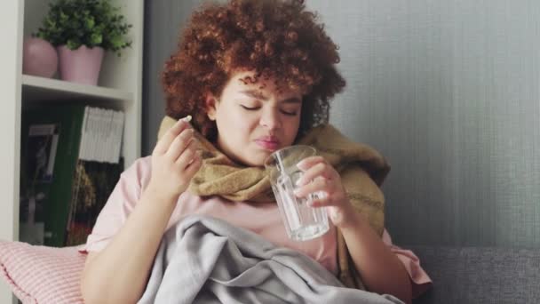 Nemocný africký americký dívka bere pilulky s vodou, ležící na gauči. — Stock video