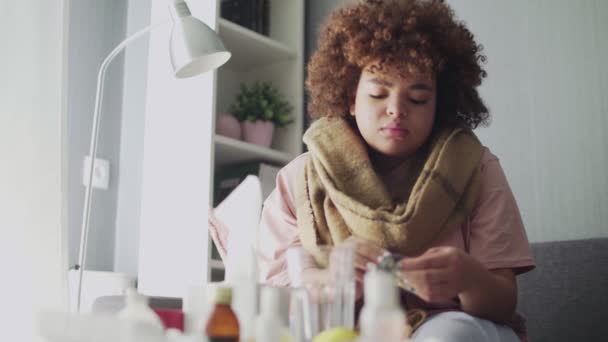 Sick african american girl takes pills with water, lying on the couch. — Stock Video