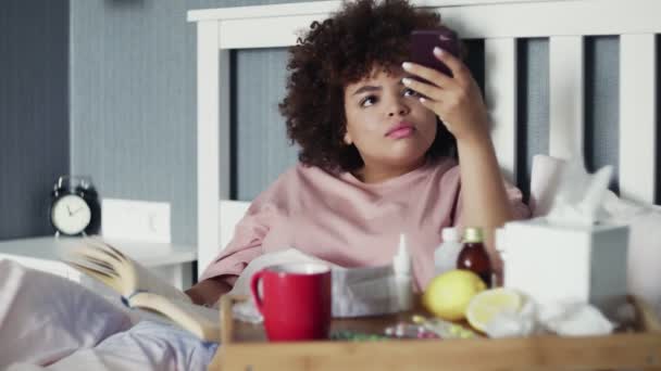 Ziek jong Afrikaans Amerikaans meisje ligt in bed en met behulp van de telefoon om een video of verhalen te maken — Stockvideo