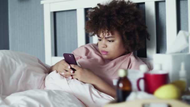 Doente Jovem afro-americana usando telefone na cama em casa — Vídeo de Stock