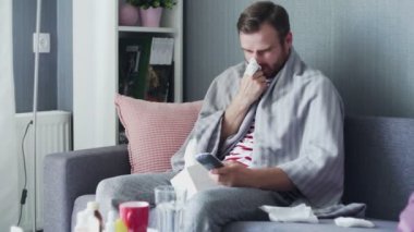 Evde grip olmuş hasta bir adam, ateşi olan bir genç adam televizyon seyrediyor ve uzaktan kumanda kullanıyor..