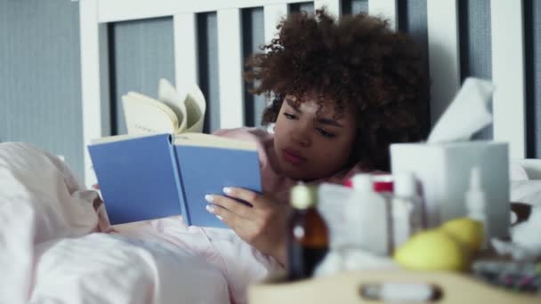 Una ragazza afroamericana malata ha il raffreddore a casa. Sdraiato a letto con un libro — Video Stock