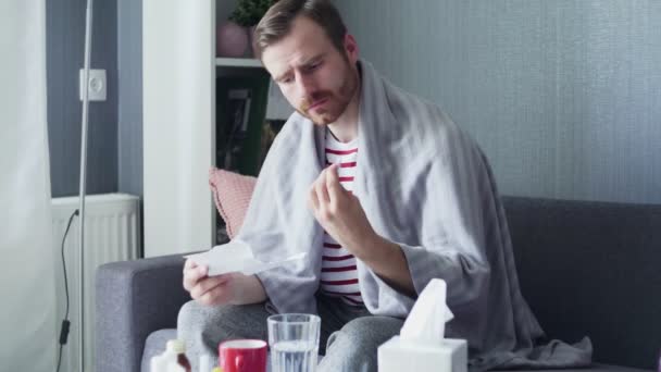 Ein erwachsener Kranker sitzt auf dem Sofa und nimmt Tabletten mit Wasser — Stockvideo