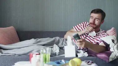 Evde grip olmuş hasta bir adam, ateşi olan bir genç adam televizyon seyrediyor ve uzaktan kumanda kullanıyor..