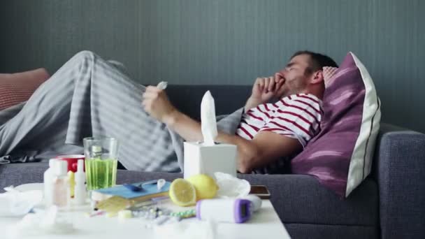 Ein kranker junger Mann versucht, während einer Krankheit auf einem Sofa in einer Wohnung unter einer warmen Decke einzuschlafen. — Stockvideo