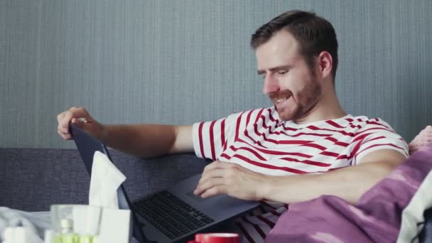 Nemocný vousatý muž pomocí notebooku a foukání nos s kapesníkem — Stock video