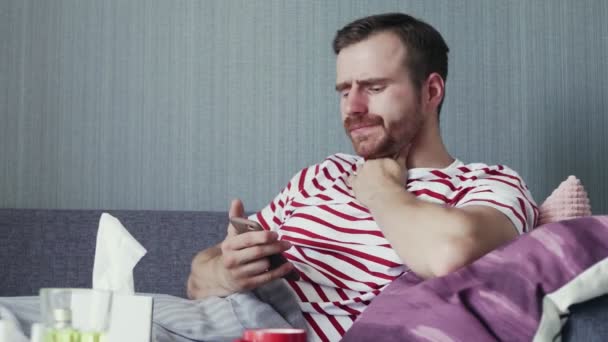 Хворий молодий чоловік використовує телефон і дме ніс з носовичкою — стокове відео