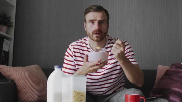 Joven, guapo hombre de negocios viendo la televisión y desayunando en la habitación de hotel — Vídeo de stock