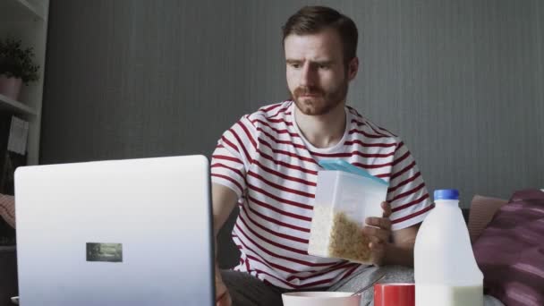 Hombre barbudo preparando el desayuno y utilizando un ordenador portátil — Vídeos de Stock