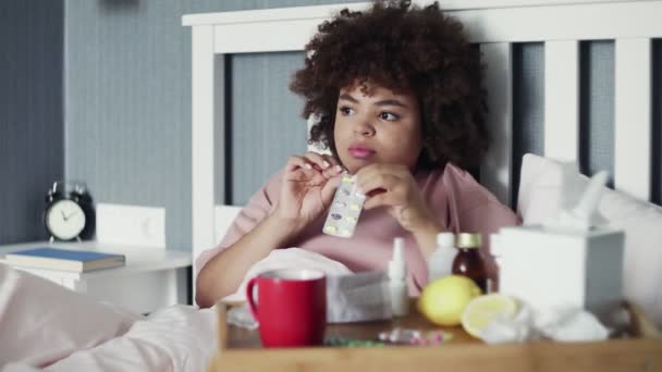 Enfermo afroamericano chica toma pastillas con agua, acostado en la cama en casa — Vídeo de stock