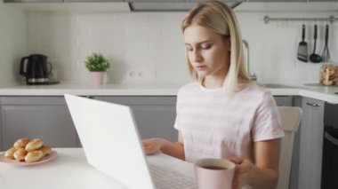 Freelancer kahve içiyor ve mutfakta dizüstü bilgisayar kullanıyor. İş kadını defter üzerinde çalışıyor