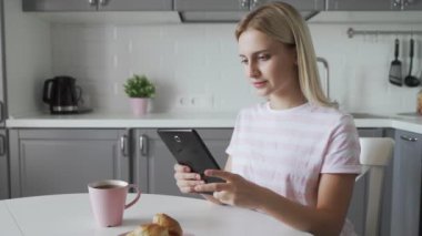 Çekici bir kadın mutfakta kahvaltı yaparken tablet kullanıyor.