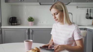 Mutfakta kahvaltı yaparken tablet kullanan üzgün kadın.