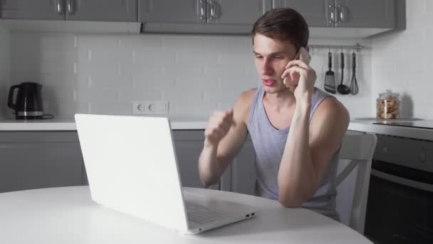 Freelancer hablando por teléfono móvil y trabajando en notebook en la cocina . — Vídeo de stock