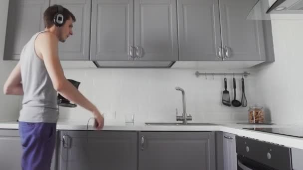 Joven cocinando el desayuno y escuchando música en los auriculares — Vídeo de stock