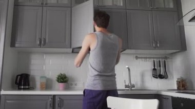 Genç adam mutfakta kahvaltı hazırlıyor. Bir kaseye mısır gevreği döker.