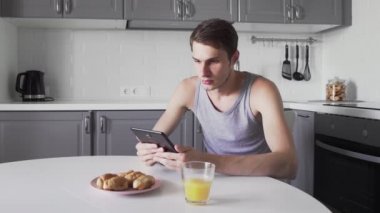 Genç adam evde mutfakta otururken dijital tablet kullanarak haberleri okuyor.